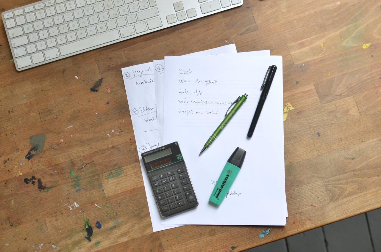 testimonials-img Top view of paper sheets with notes placed with pens with calculator and marker near keyboard on dirty table